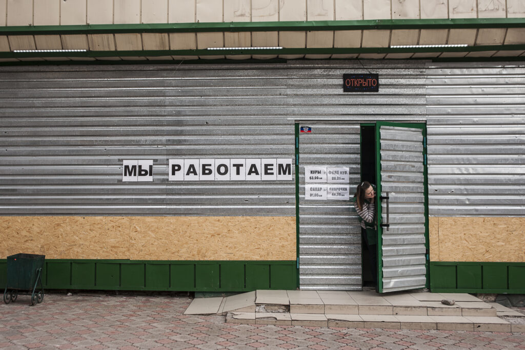 Una dona treu el cap per la porta d’una tenda. Tots els negocis es troben folrats amb metalls o fustes per intentar salvar les finestres dels bombardejos. Al cartell, hi diu: ‘’Estam treballant’’.